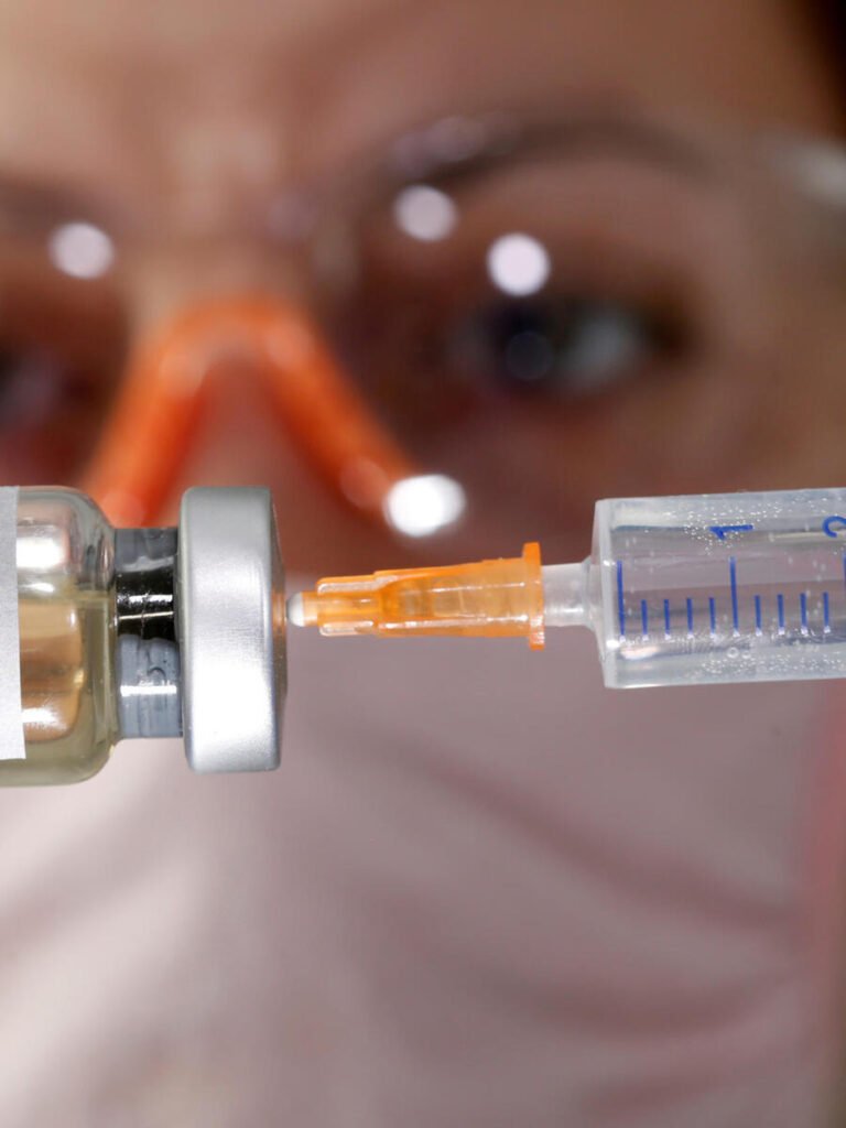 A woman holds a small bottle labeled with a "Vaccine COVID-19" sticker and a medical syringe in this illustration